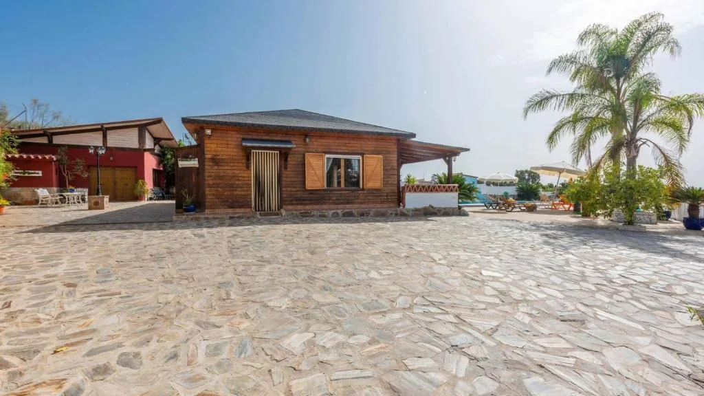 Fachada de Cortijo La Tata, casa de madera con porche cubierto sobre un patio empedrado
