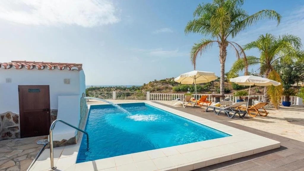 Piscina privada de Cortijo La Tata en Almayate Alto, con tumbonas, palmeras y vistas a la campiña hasta el horizonte