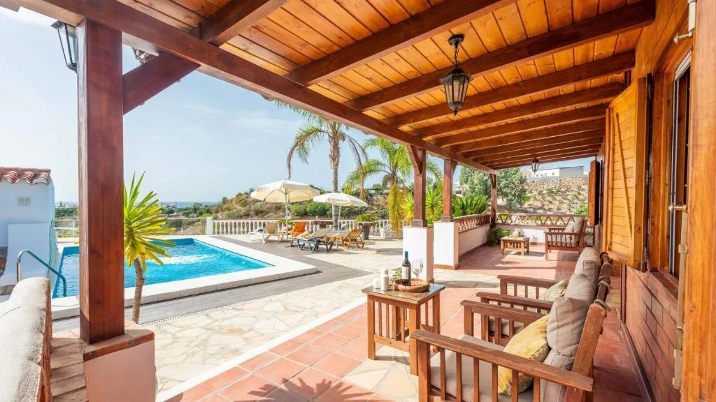 Porche cubierto de Cortijo La Tata con vistas a la piscina, tumbonas y la campiña de la Axarquía